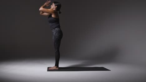 Studio-Shot-Of-Mature-Woman-Wearing-Gym-Fitness-Clothing-Standing-On-Mat-Doing-Variety-Of-Pilates-Stretching-Exercises